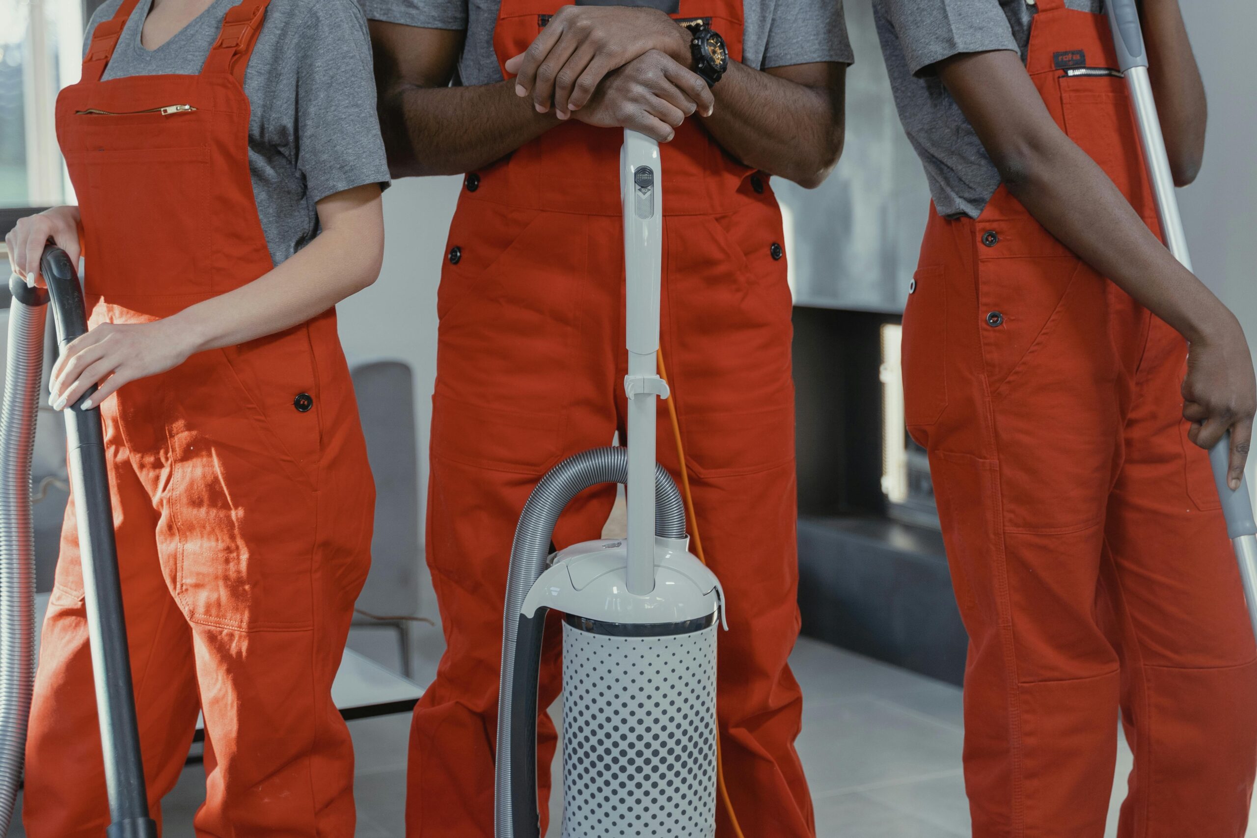 Three workers in red coveralls with cleaning tools in a room.